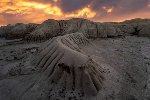 A dramatic sunset illuminates the layered rock formations at Bisti/De-Na-Zin Wilderness in New