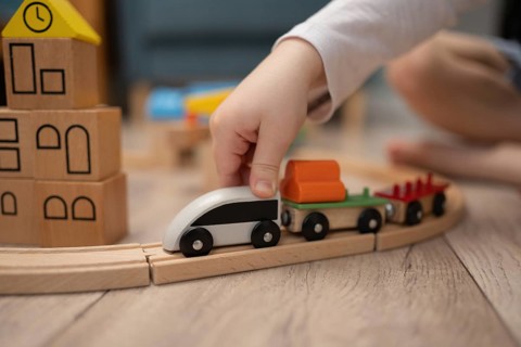 A child hand guides a wooden toy train along a curved track, surrounded by colorful building blocks