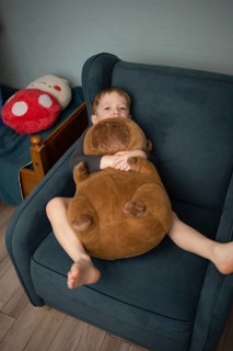 A child relaxes in a cozy chair, cuddling a large plush bear. The scene exudes comfort and warmth,