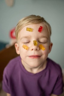 A child with closed eyes smiles blissfully with colorful gummy bears on their face, expressing a