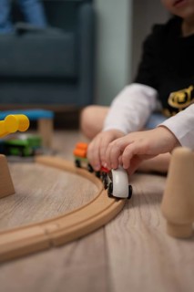A child sits on the floor, immersed in playing with a wooden train set. The soft focus emphasizes