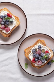 Top view of two toasts with cream cheese topped with raspberries, blueberries, and dusted with