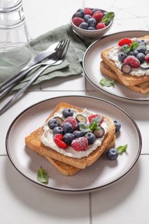 Plated serving of toast layered with cream cheese and topped with an assortment of fresh berries