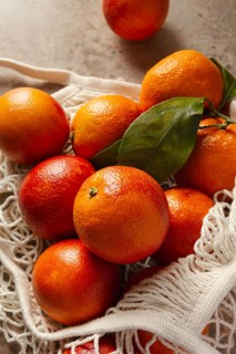 A bunch of vibrant blood oranges with deep red hues sit in a reusable cotton bag on a rustic table.