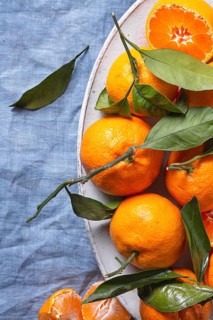 Fresh tangerines with vibrant green leaves are artfully arranged on a textured blue fabric,