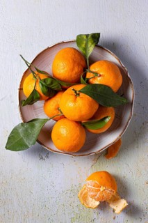 A vibrant arrangement of fresh tangerines with green leaves, displayed on a rustic plate against a