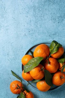 Fresh tangerines with vibrant green leaves arranged on a textured blue surface, creating a visually
