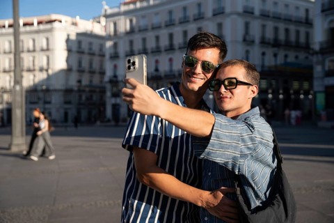 A gay couple joyfully captures a selfie on the vibrant streets of Madrid. The warm sunlight