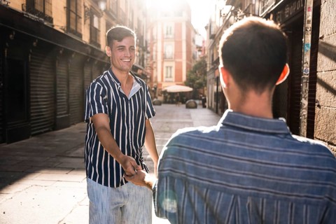 A joyful gay couple holds hands while strolling through the charming sunlit streets of Madrid.