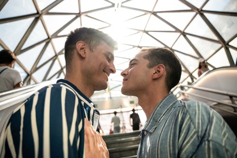 A gay couple shares a tender moment on the streets of Madrid. The sun sets behind them,