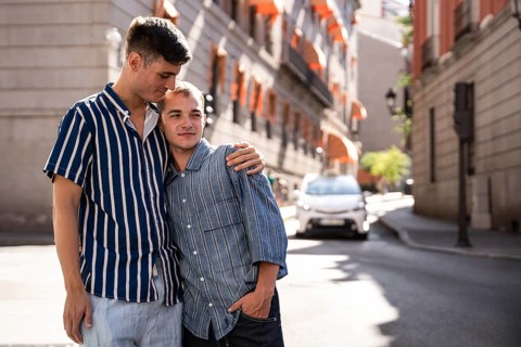 A joyful gay couple embraces in the sunny streets of Madrid, celebrating love and togetherness. The