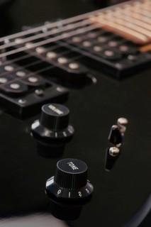 Detailed view of a black electric guitar volume and tone knobs, with strings visible. The image