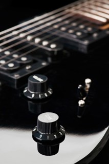 Close up image showcasing the knobs and strings of a black electric guitar, focusing on details