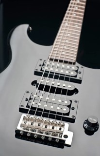 Close up image of a black electric guitar showcasing its strings, pickups, and volume knob. The