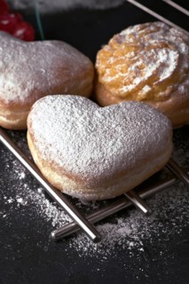 A close up of delectable heart shaped cream buns, generously dusted with icing sugar, presented on