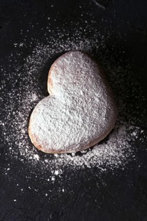 Top view of a delicious heart shaped cream bun generously dusted with icing sugar, presented on a