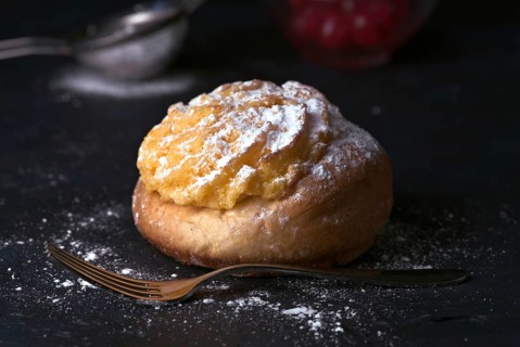 A delectable cream bun sprinkled generously with icing sugar, sitting beside a vintage fork on a