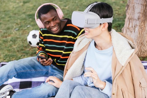 Two friends enjoy a sunny day at the park, one wearing a virtual reality headset, while the other