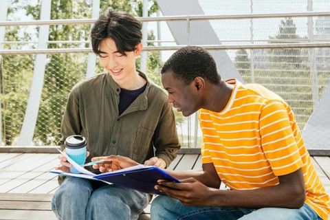 Two students friends studying together outdoors, discussing notes and sharing ideas. They are