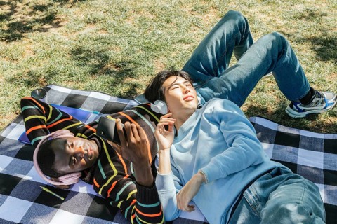 Two friends enjoy a sunny day in the park, lying on a checkered blanket. They are wearing
