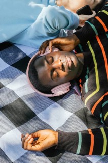 Friends relaxes on a checkered blanket, wearing headphones and basking in the sunlight. The