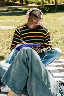 Friends sits on a checkered blanket in the sun, wearing headphones and a striped sweater, enjoying