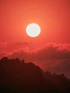 An ethereal orange sunset backlights a silhouette of mountainous terrain, expressive of untouched