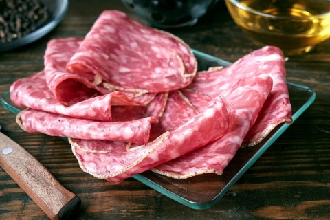 Thin slices of spanish salami are arranged on a glass plate atop a rustic wooden table. The marbled