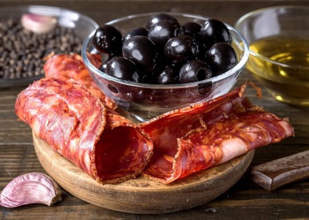 A close up of a gourmet arrangement featuring spanish chorizo, black olives in a glass bowl, and a