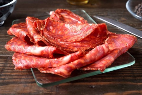 A close up shot of thinly sliced spanish chorizo arranged on a clear glass plate. The vibrant