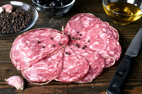 A close up view of spanish salami slices with black peppercorns on a rustic wooden table, alongside