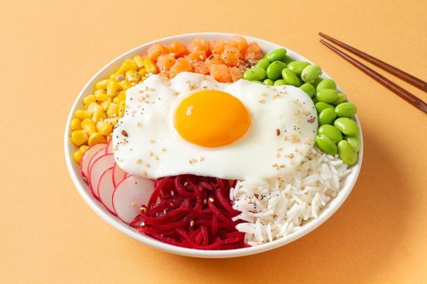 A colorful poke bowl featuring fresh vegetables, rice, and a perfect fried egg on top. Radishes,