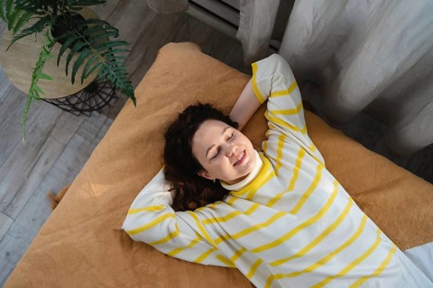 A woman lies on a brown blanket, smiling and relaxed, wearing a white and yellow striped sweater. A