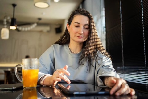 A serene middle-aged woman interacts with a tablet at a sunlit cafe table, amidst a relaxed setting