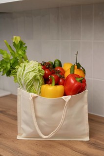 A canvas bag filled with fresh vegetables, including bell peppers, celery, and lettuce, rests on a