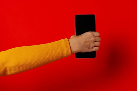 Crop hand of anonymous male demonstrating cellphone black screen against red background
