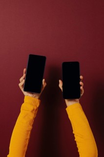 Side view of unrecognizable person in casual clothes holding smartphones with black screen while
