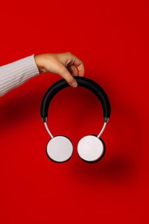 Crop anonymous person holding wireless headphones over red background