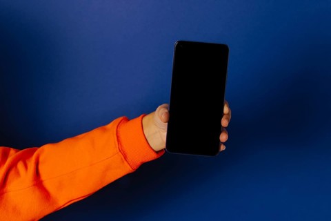 Crop hand of anonymous person holding smartphone with black screen against blue background