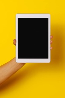 Crop hand of anonymous male demonstrating tablet black screen against yellow background