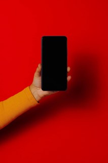 Crop hand of anonymous male demonstrating cellphone black screen against red background