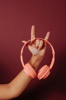 Crop anonymous woman holding headphones and making the rock sign over dark red background