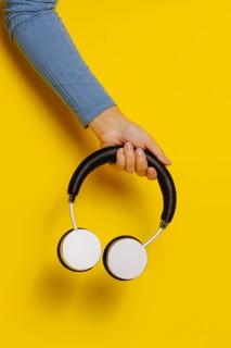 Crop hand holding headphones on yellow background