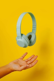 Crop anonymous person holding levitating headphones on yellow background