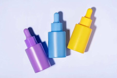 Top view of three vibrant-colored cosmetic serum bottles in purple, blue, and yellow neatly