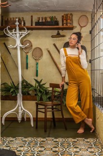A young woman engages in teleworking, standing while using a smartphone, dressed in bold mustard