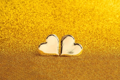 Two golden heart-shaped objects set against a shimmering golden backdrop, ideal for St. Valentine's