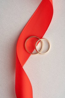 Two elegant gold wedding rings lying on a bold red ribbon, captured on a textured white backdrop. A