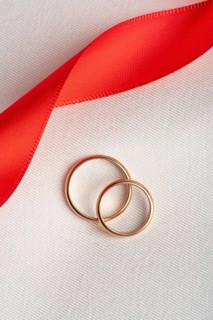 Top view of two golden wedding rings lying on a textured white fabric, intertwined with a vibrant