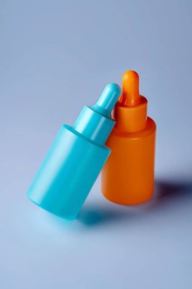 Two vibrant serum bottles in blue and orange hues are showcased against a soothing blue background,